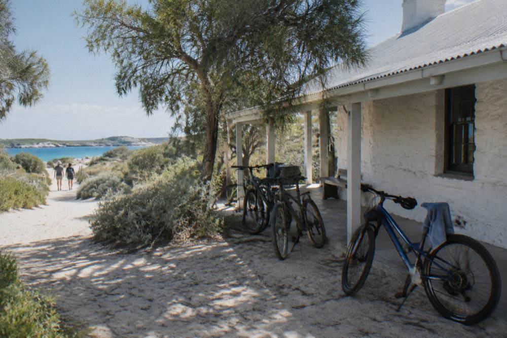 Bicycles parked on a sandy path near white heritage buildings in the settlement